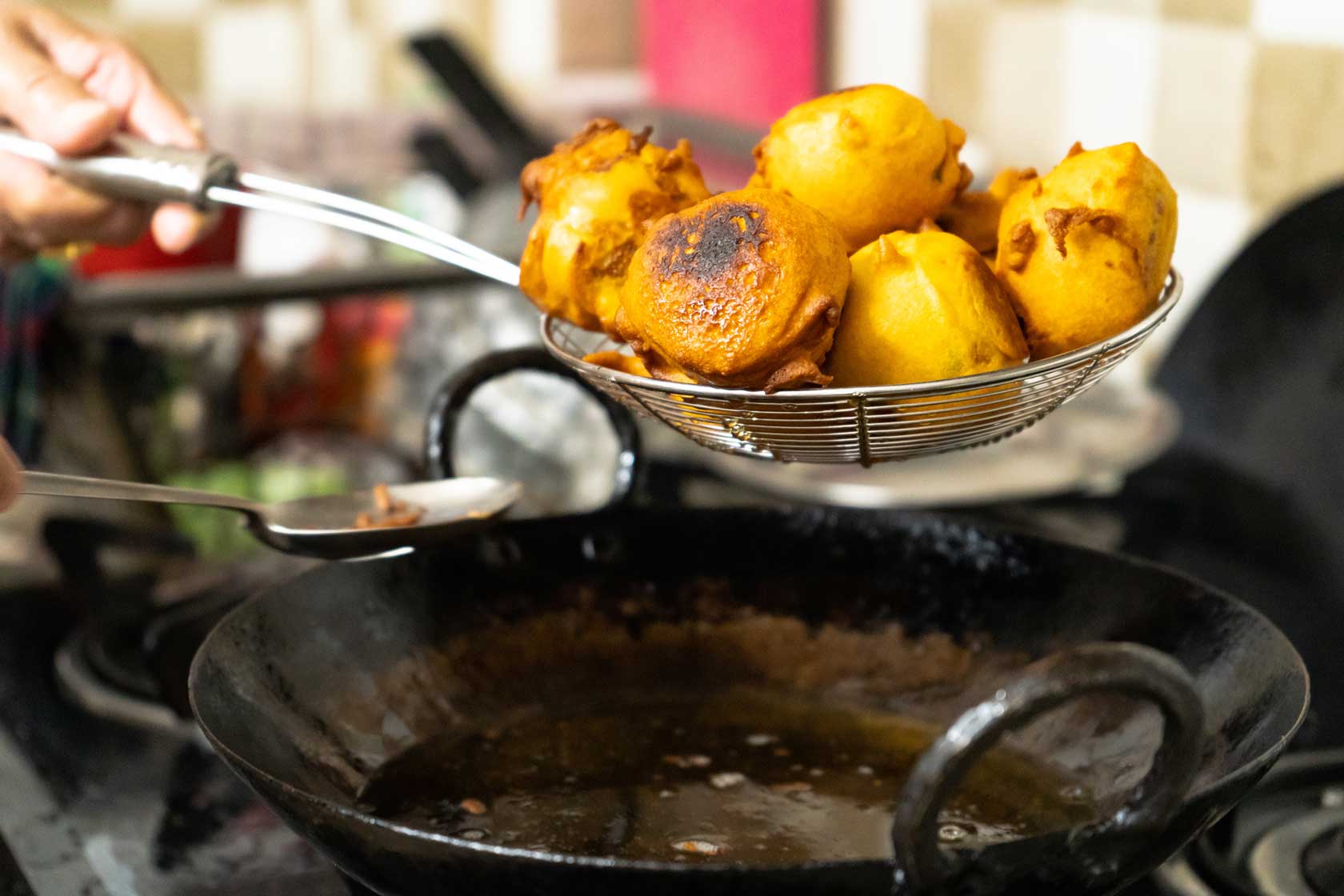 Vada potatoes wrapped in flour being taken out of hot oil after deep frying