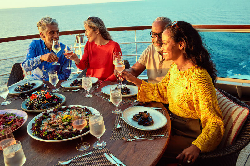 A happy group of Seabourn passengers enjoy dinner on the deck as the sun sets.