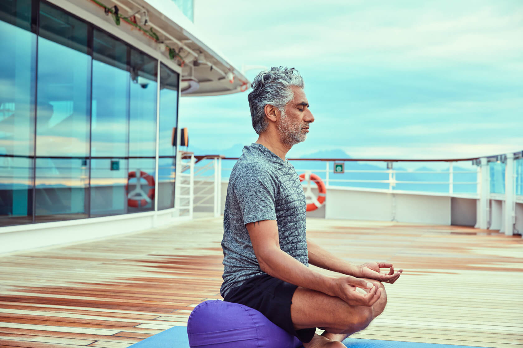 Under blue skies, a man practices meditation on the Seabourn Cruise Ship.