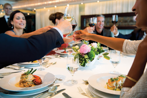 Seabourn passengers toast their glasses of wine over an elegant meal.