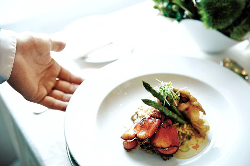 A waiter's hand sets an elegant dish to the table.